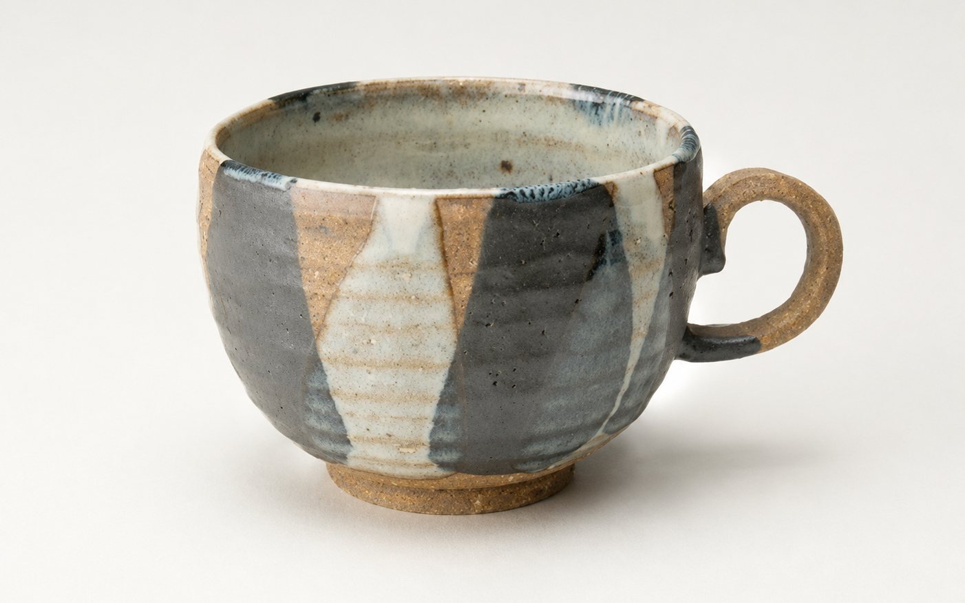 A hand-thrown stoneware cup glazed in slate grey and cream over bare clay